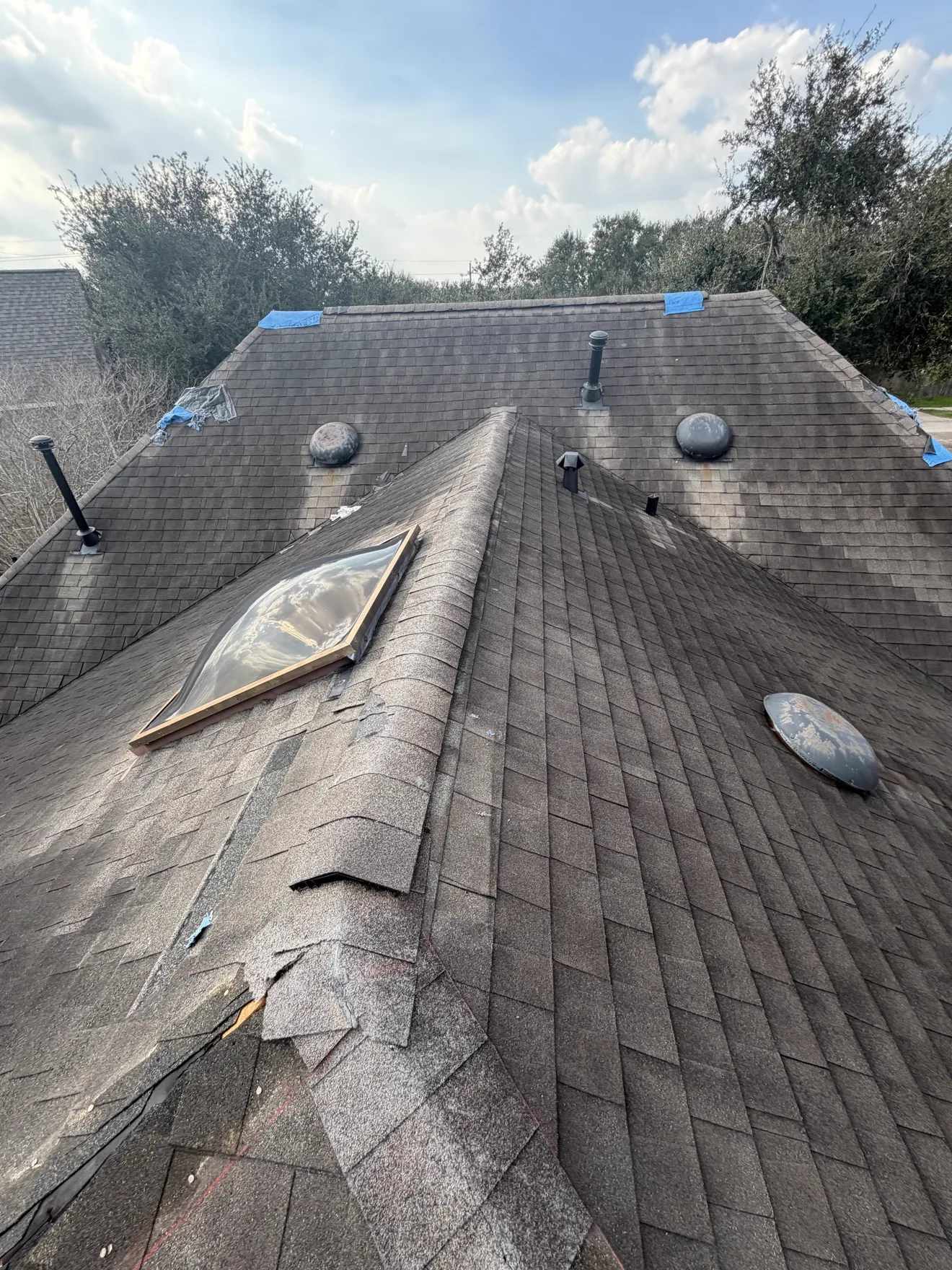Roof inspection with damage areas marked in blue tape near a skylight