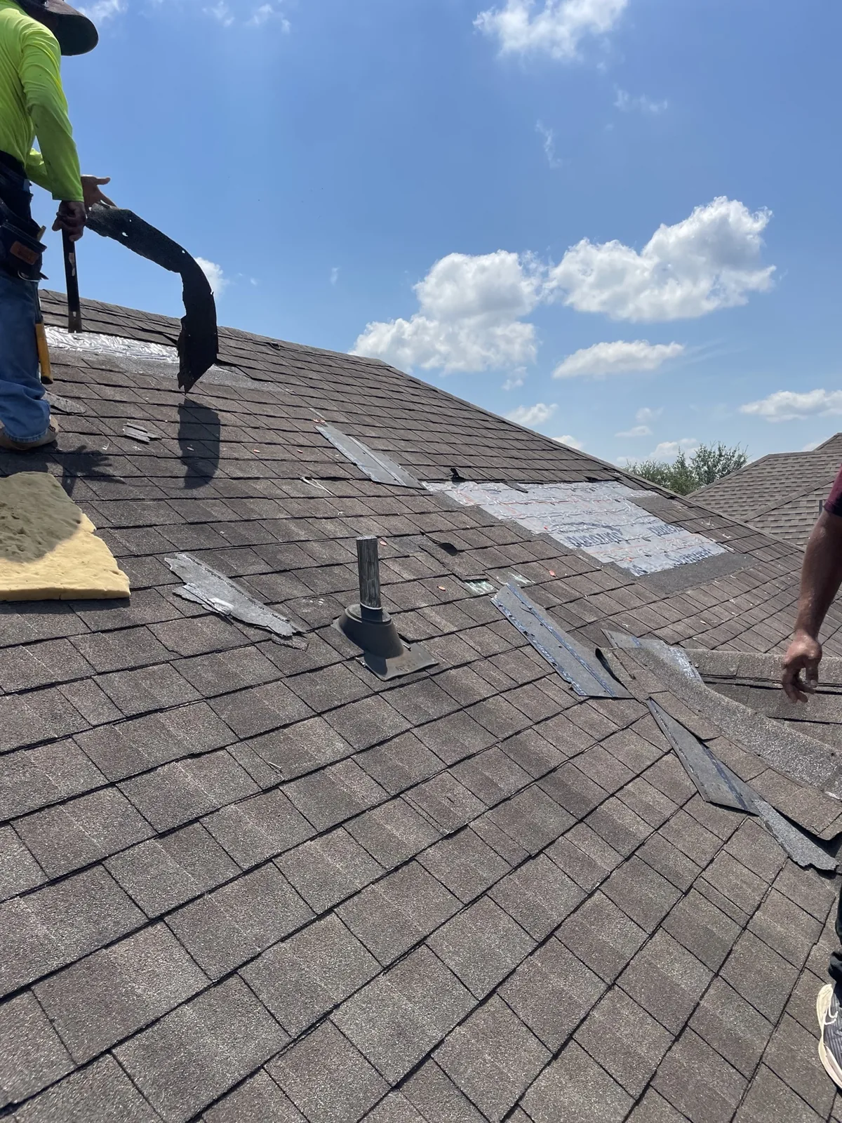 Crew member tearing off old shingles during a roof replacement